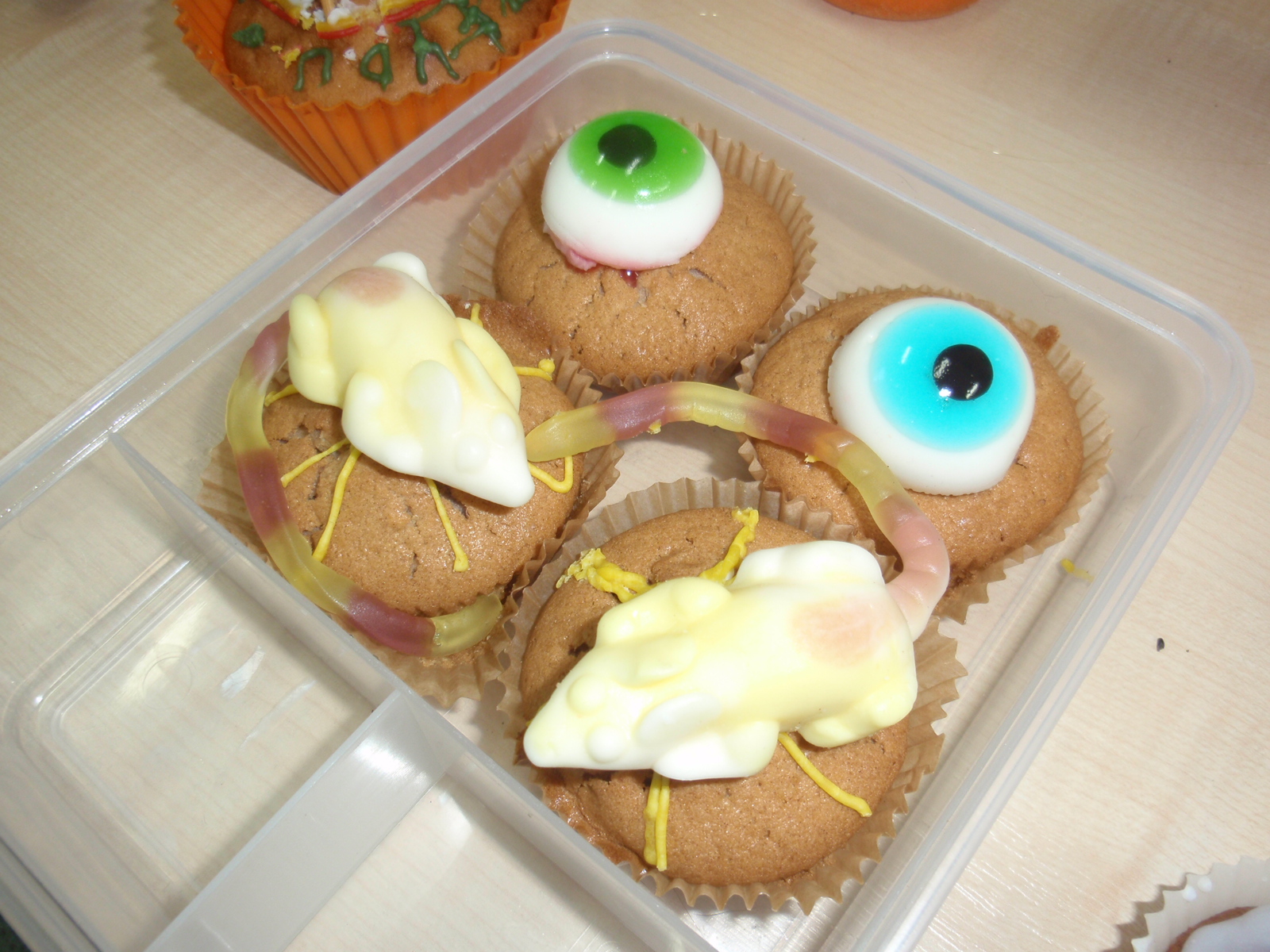 pudełeczko ,w którym są 4 ciastka i – 2  imitujące ludzkie oko oraz 2 przedstawiające myszy na ciastku.