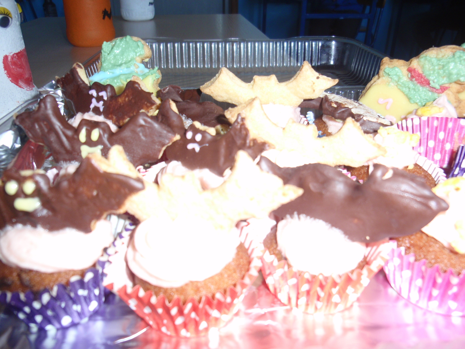 Na zdjęciu są ciastka w pudełku   -ciastka ozdobione są figurkami nietoperzy  z  czekolady i ciasta w żółtym kolorze. 