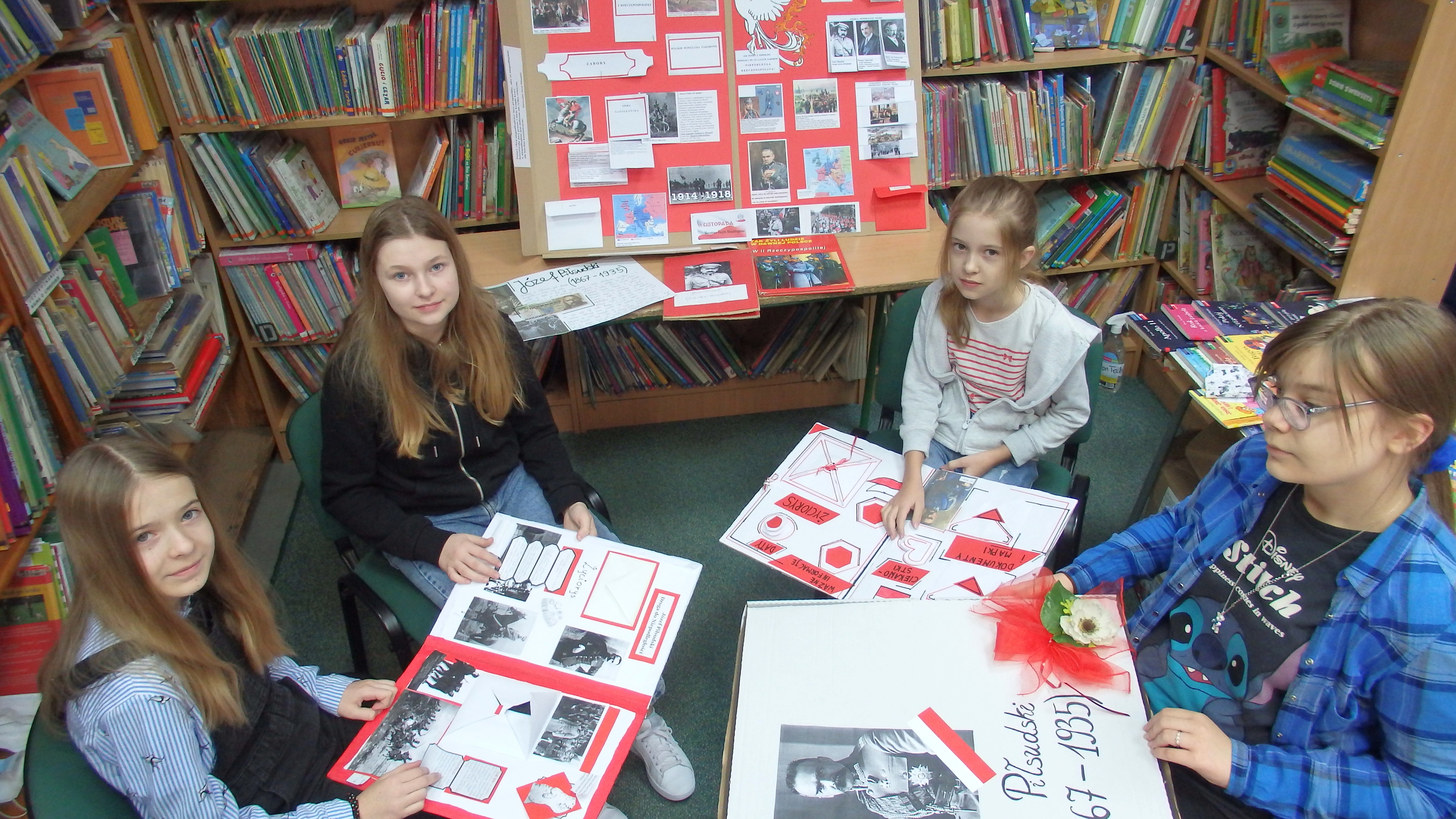 W bibliotece 4 uczennice z klasy VII c prezentują wykonane przez siebie Lapbooki czyli książki wykonane w tonacji biało-czerwonej. Temat : Józef Piłsudski.